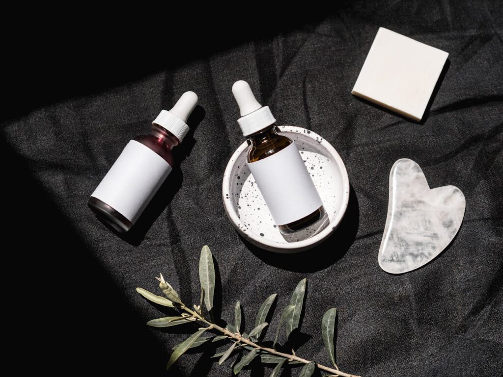 Brown Glass Bottles on Black Textile Beside Gua Sha and Bar Soap